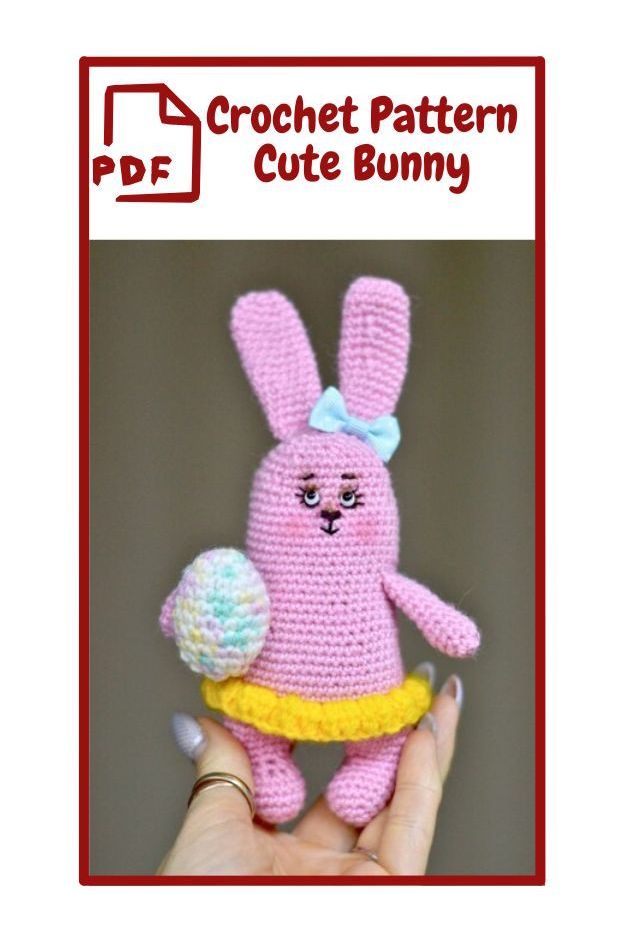 The image shows a crochet pattern for a cute bunny. The bunny is crocheted in pink yarn and has long ears. It is wearing a yellow skirt and has a light blue bow on its head. The bunny is holding a multicolored crochet egg. The text at the top of the image reads "PDF Crochet Pattern Cute Bunny" in red letters.   PDF  Crochet Pattern Cute Bunny   rabbit, bunny, cartoon, toy, text, rabbits and hares, domestic rabbit, easter. a person holding a stuffed animal.